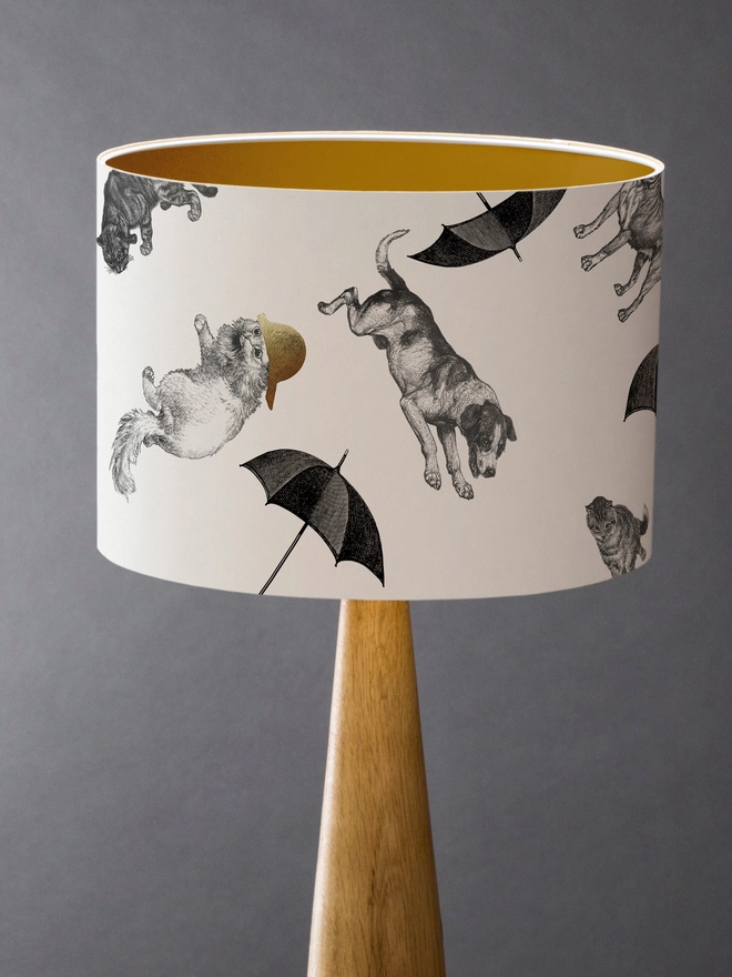 Drum Lampshade featuring cats and dogs ‘raining’ from the sky with a gold inner on a wooden base 