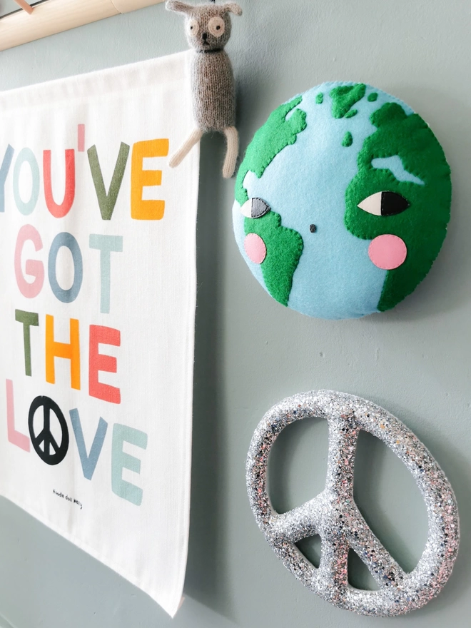 A Earth wall hanging hung up on a wall with a glitter peace sign