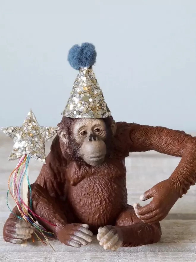 Orangutan seen in a sparkly hat with a blue pom pom.