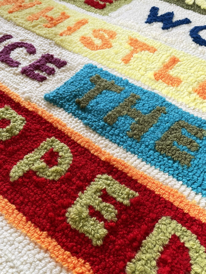 Close up of typographic punch needle textile art "She missed the wolf whistles once they stopped" in bright wool type with coloured block backgrounds