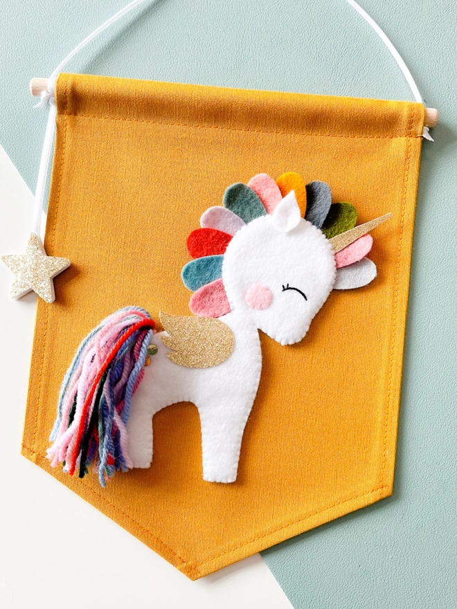 A white unicorn on a mustard coloured fabric banner