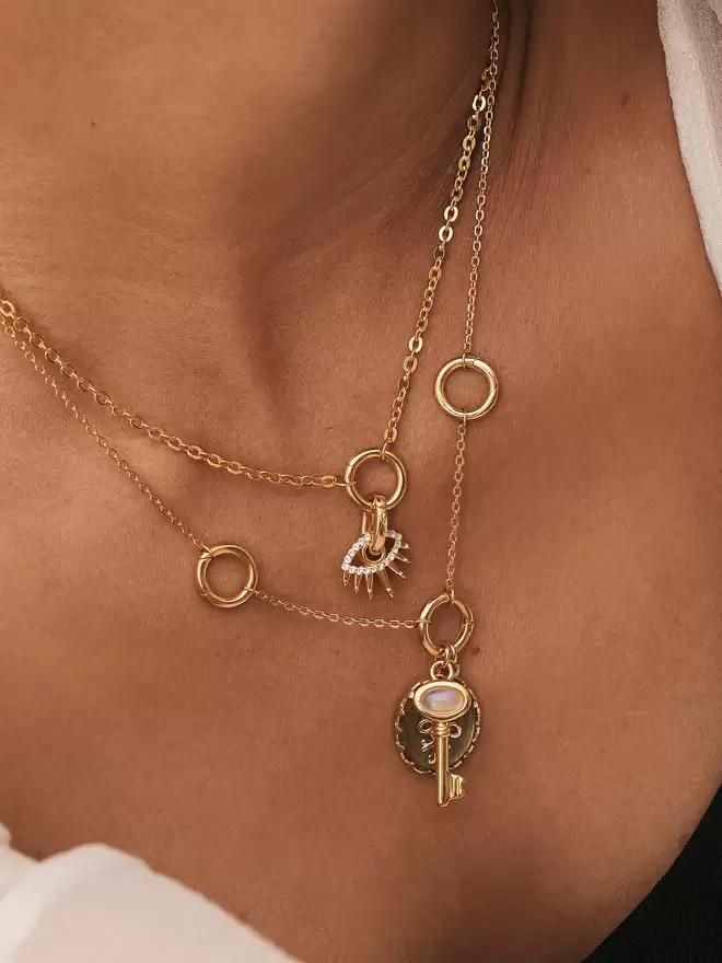 woman wearing two gold necklaces styles with an evil eye gold charm, a skeleton key with moonstone and a labradorite three keys pendant