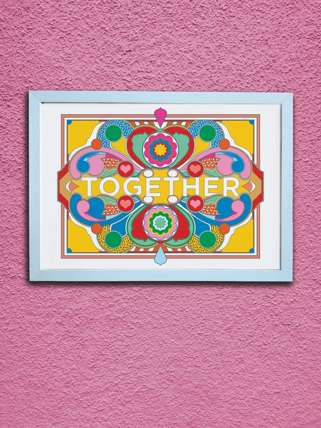 A landscape print on a white background with dark blue linework and green, blue red pink and gold sections. Across the centre of the image is written ‘TOGETHER’. It is in a white frame hung on a textured pink wall.