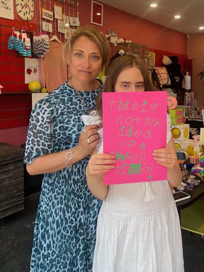 Piper with her mum Kate. Piper is holding up a copy of her print which has her handwritten unique font in green on a bright pink background