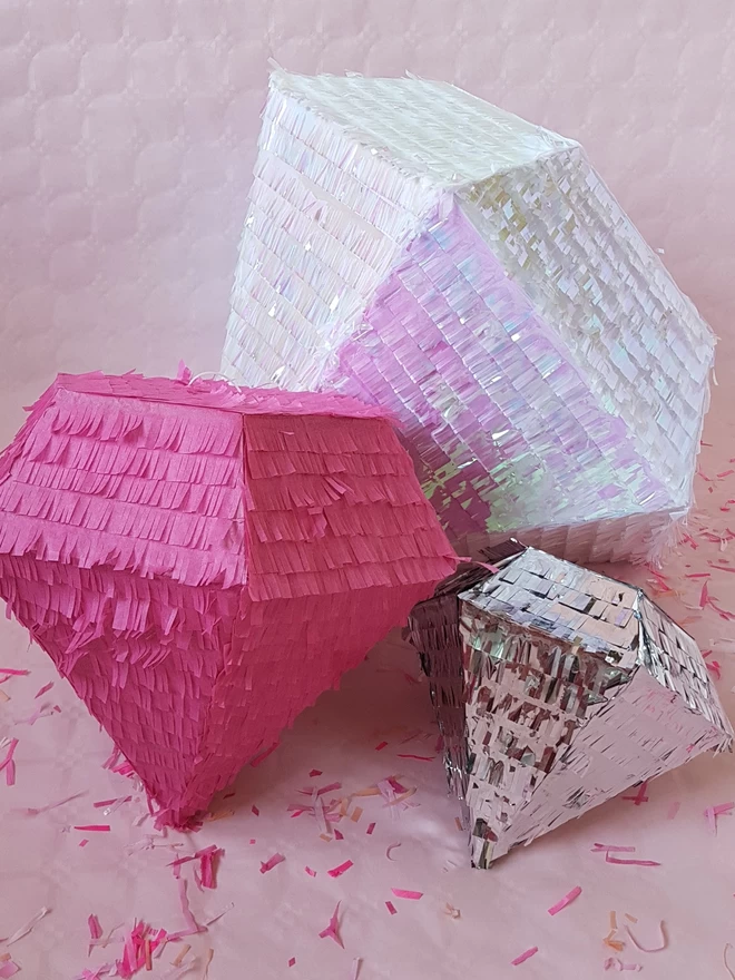 Trion of different size diamond pinatas on a pink background