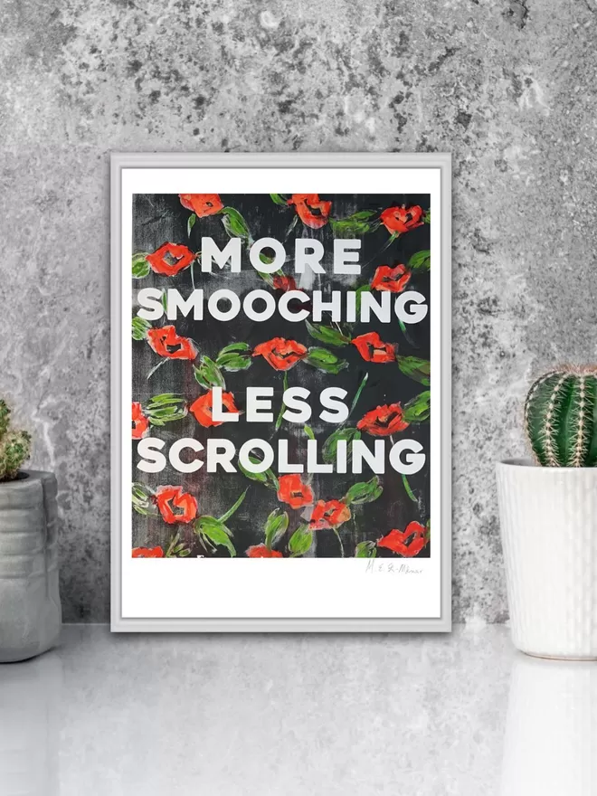 MORE SMOOCHING, LESS SCROLLING fine art print.  Based on an original monoprint by M.E. Ster-Molnar.  Shown on a grey concrete wall with a cactus plant.  