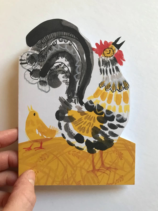 Shaped Crowing Cockerel greetings card illustrated by Esther Kent in in yellow and black, stands against a white background