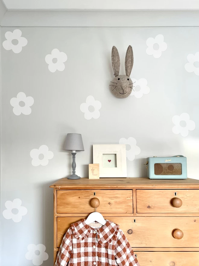 White flower wall stickers in girls bedroom with gingham jacket, chest of drawers, lamp and radio