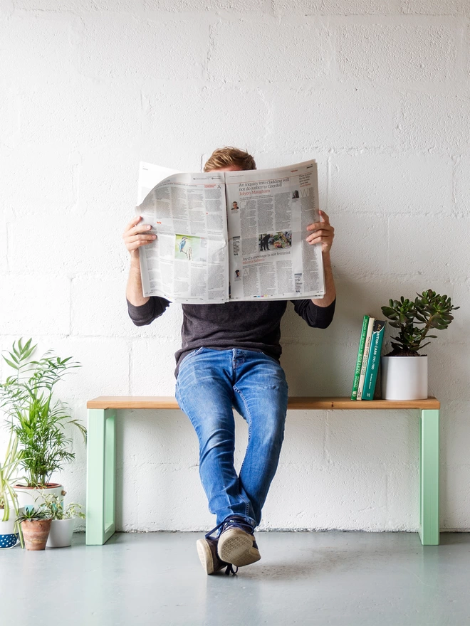 man sat reading newspaper on a stylish hallway bench with pistachio green boxy steel legs, surrounded by house plants