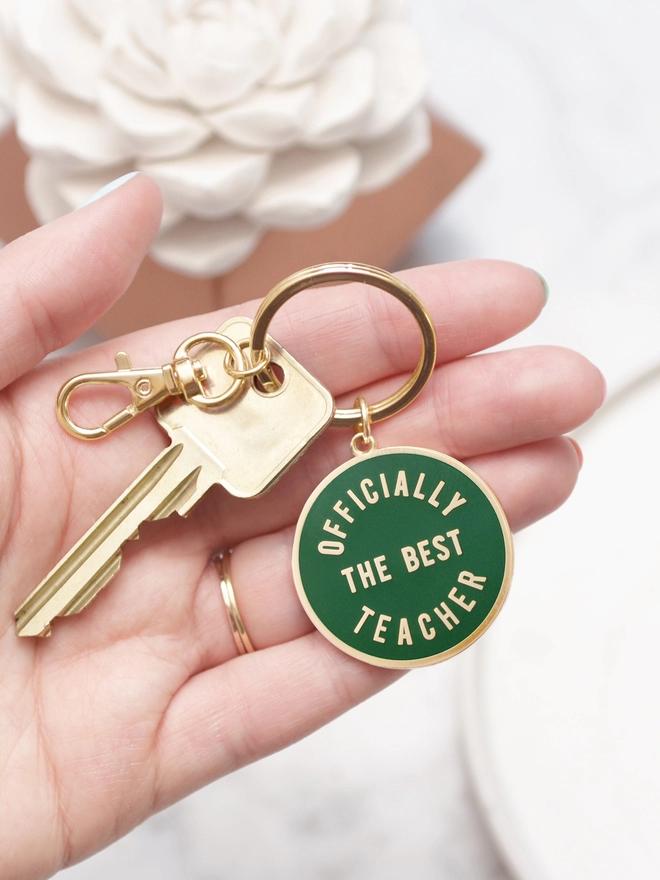 hand holding a green keyring with 'officially the best teacher' design