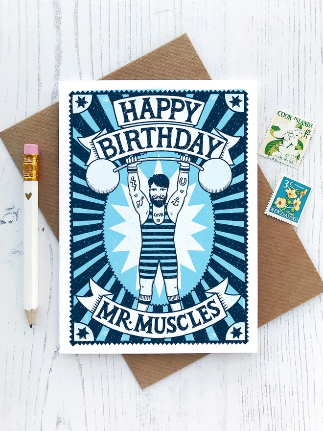 blue mr muscles muscle man birthday card with brown envelope and stamps and white pencil