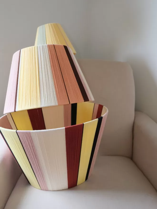 Lifestyle image of lampshade stack on an armchair with Warm Neutrals lampshade in the middle.