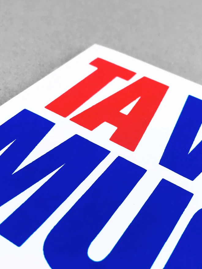 A close up of the red and blue lettering, the TA in red is at the topand then partially legible blue letters around it. The card is at a slight angle, showing the light grey background beyond.