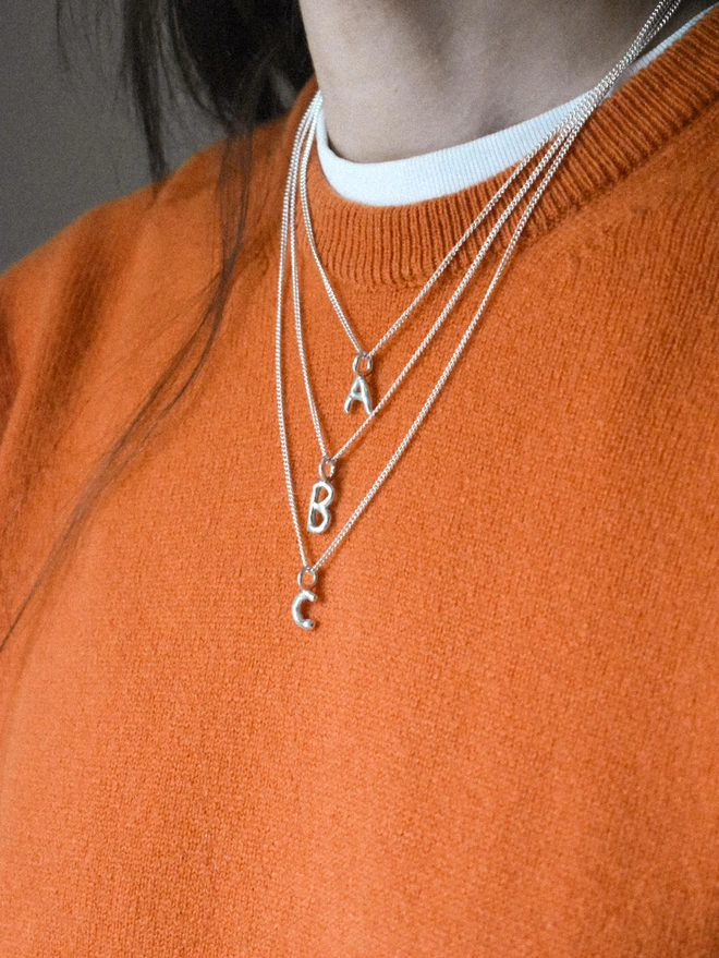 a model wears three lengths of slinky chain, 16", 18" and 20" with wobbly alphabet pendants, showing the difference in each length of chain.
