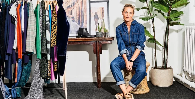 Mandy Watkins, founder of Hush, looking at the camera, wearing a denim jumpsuit, sat next to a rack of Hush products.