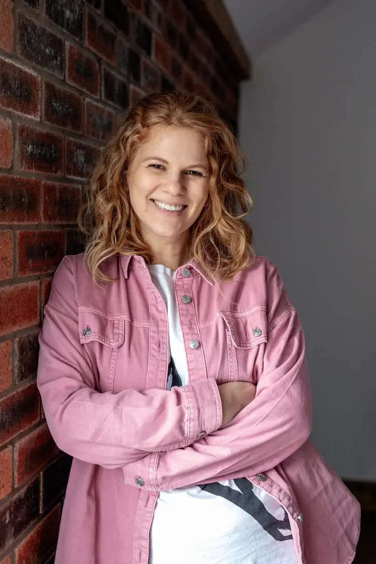 Ella Fletcher smiling in a pink jacket, leaning against a brick wall