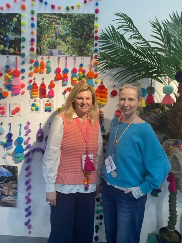 kat and marisa standing together in front of a wall of pom pom products and garlands