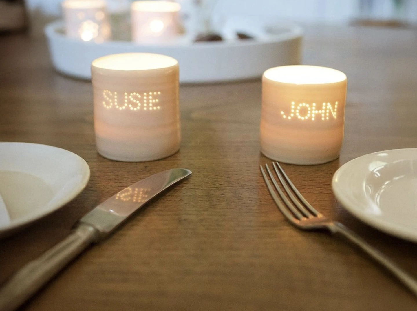 Personalised ceramic tea light holder. A ceramic tea light holder on a table with two names stamped on the front.