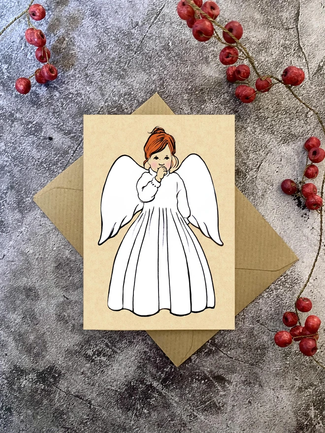 a7 size greeting card featuring an illustration of an angel sucking her thumb with red hair and a Kraft envelope