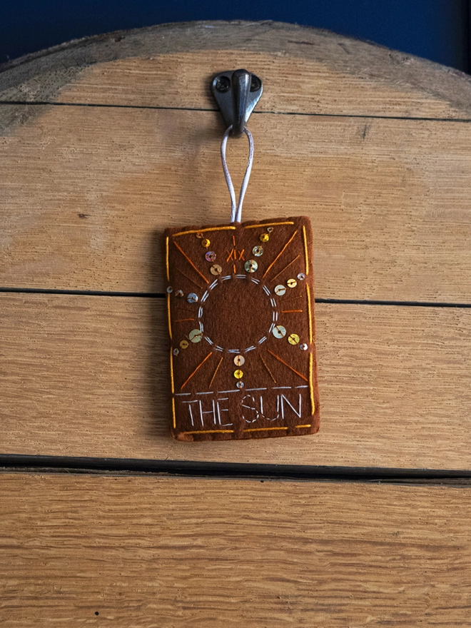 A handcrafted felt ornament with sequins and embroidery depicting "The Sun" tarot card.