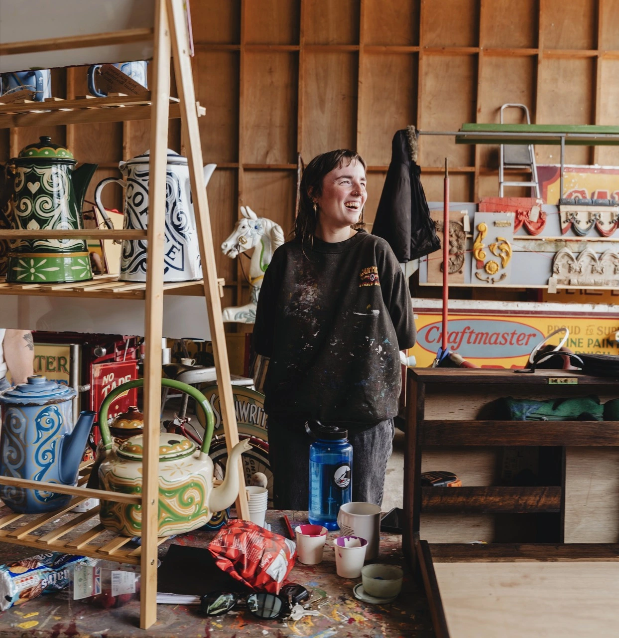 Jess Grimsdale standing in fairground workshop with enamel teapots