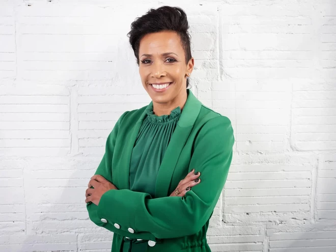 Kelly Holmes, olympian athlete, smiling at the camera with her arms crossed in a green suit.