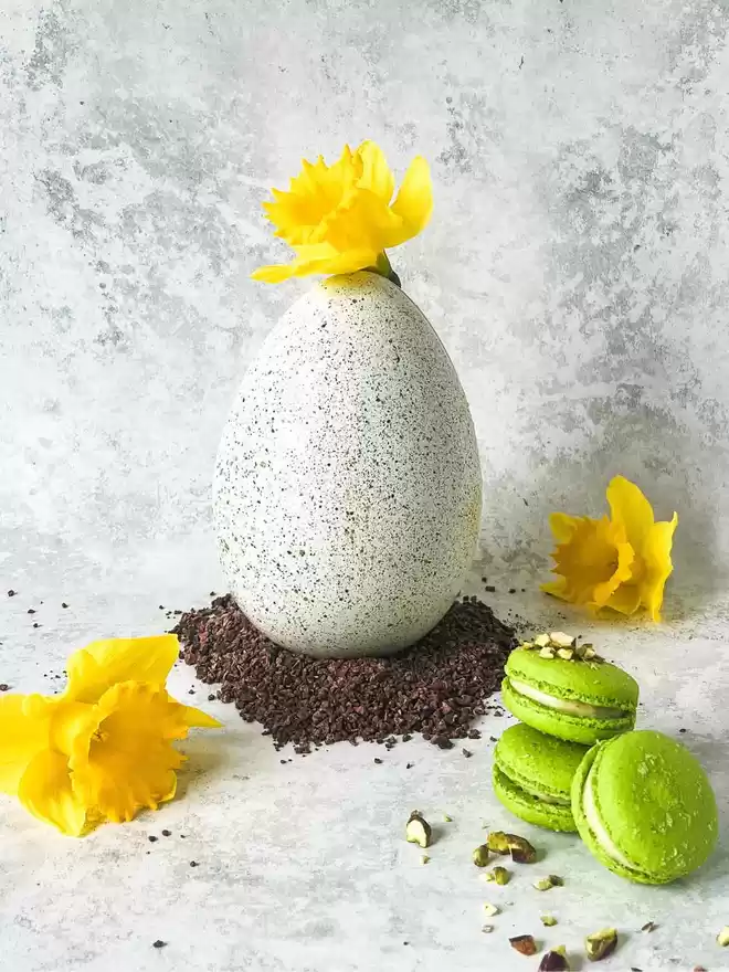 a green speckled pistachio easter egg with flowers and green pistachio macarons on a table