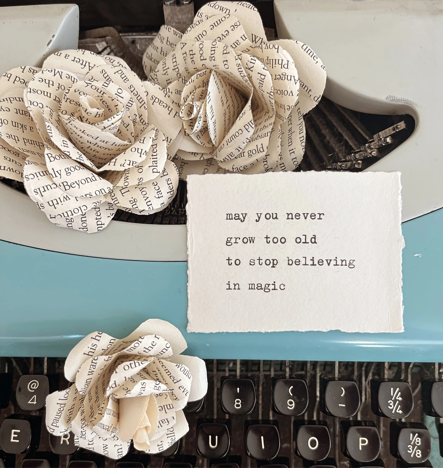 image of a typewriter with handmade book origami flowers and a typewriter quote on handmade paper reading 'may you never grow too old to stop believing in magic'. 