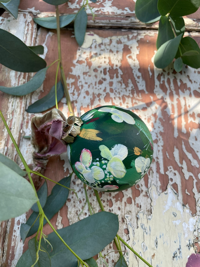 hand painted ceramic christmas bauble deep green background adorned with white hydrangeas. 