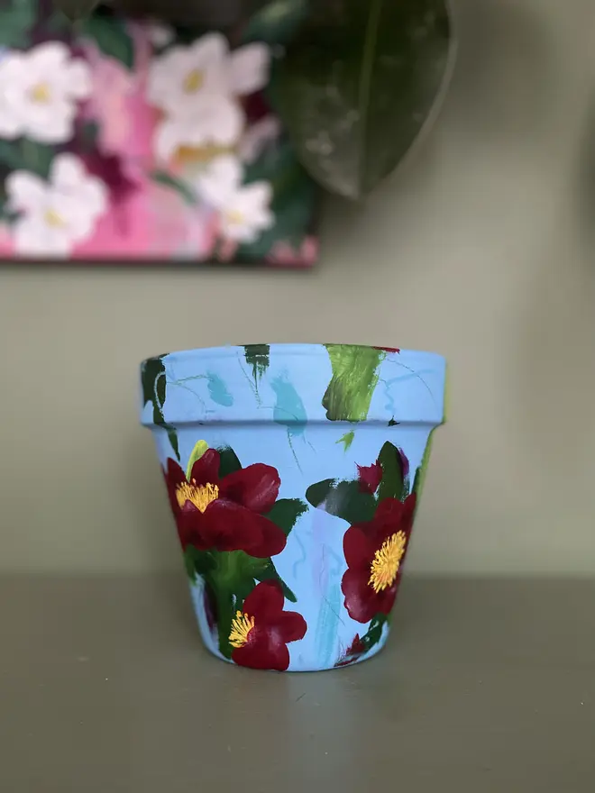 Vibrant hand painted floral plant pot deep red camellia flowers.