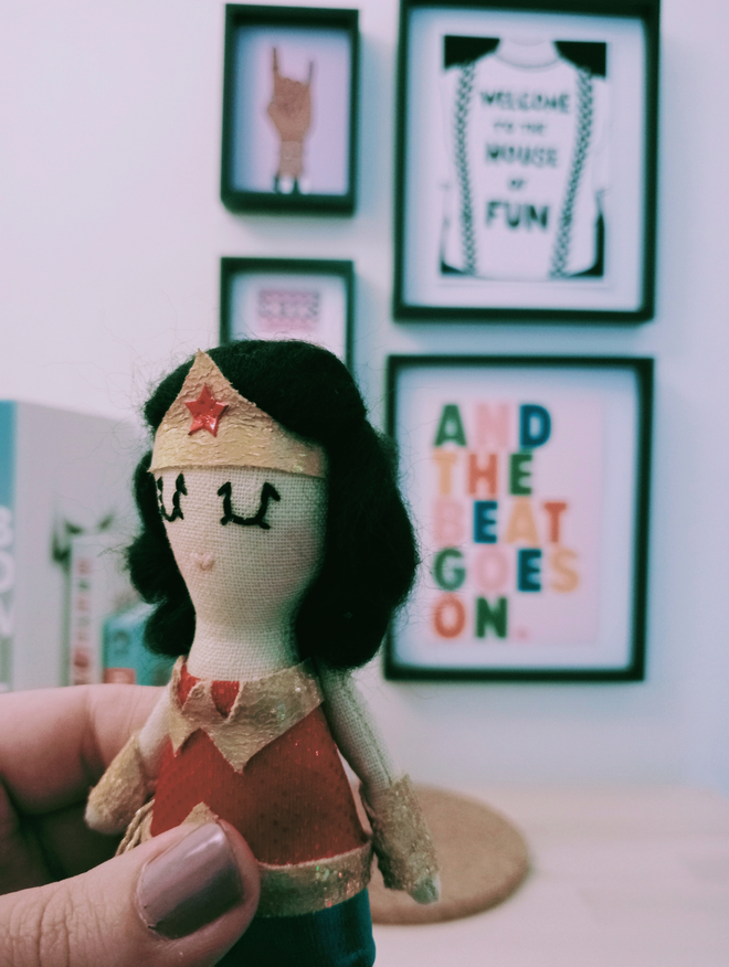 Wonder woman mini decorative icon doll vintage inspired. Held in front of a gallery wall of pop culture prints