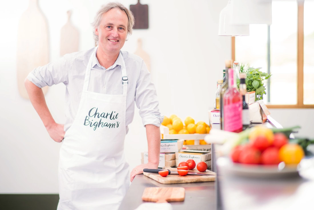 Charlie Bigham, founder of Charlie Bighams, smiling at the camera wearing a white 'Charlie Bigham's' apron.