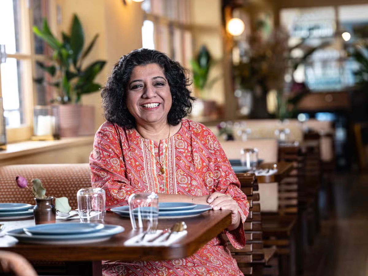 Asma Khan, founder of Darjeeling Express, smiling at the camera in a red dress.