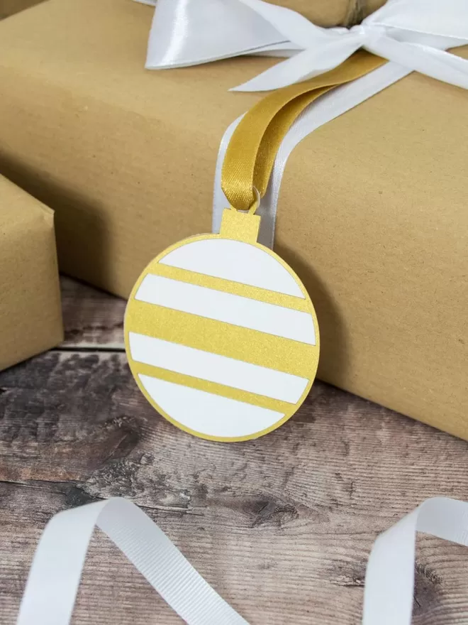 Gold and white bauble gift tag attached to present wrapped in brown paper.Gold and White Christmas Bauble Gift Tag