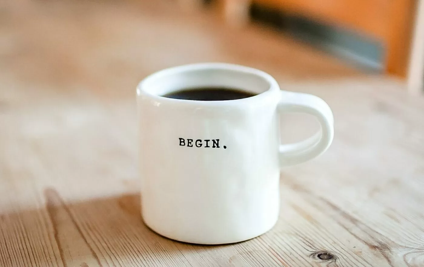 White ceramic mug with the word begin written on it sat on a wooden table