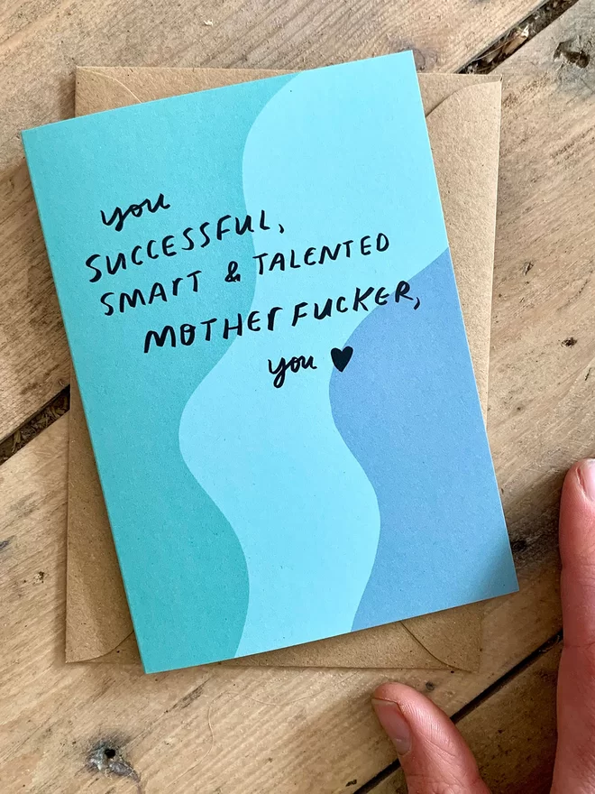 Card lies on wooden background. Reads 'you successful, smart & talented motherf*cker, you'