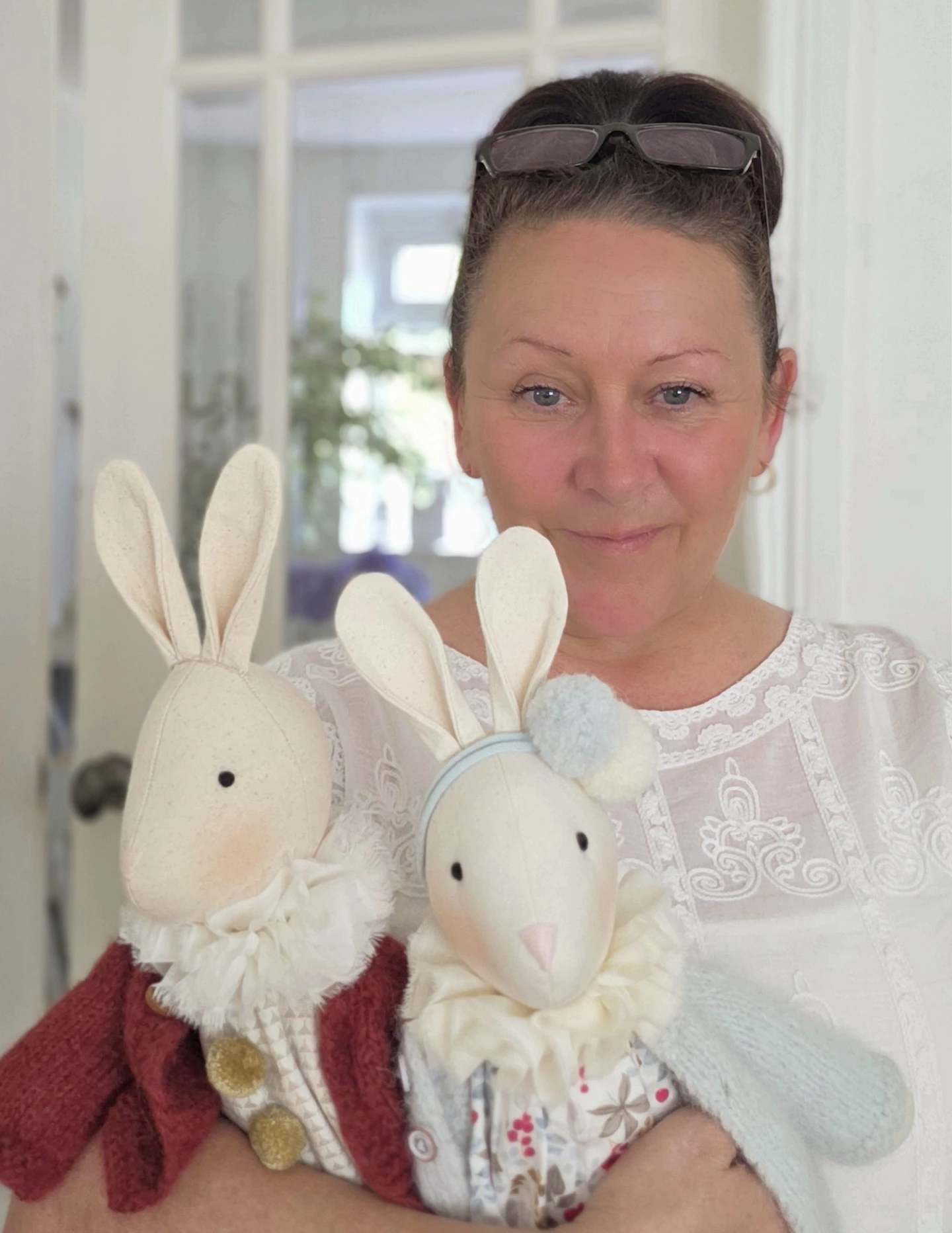 maker holding two linen bunnies dressed in whimsical heirloom clothing.