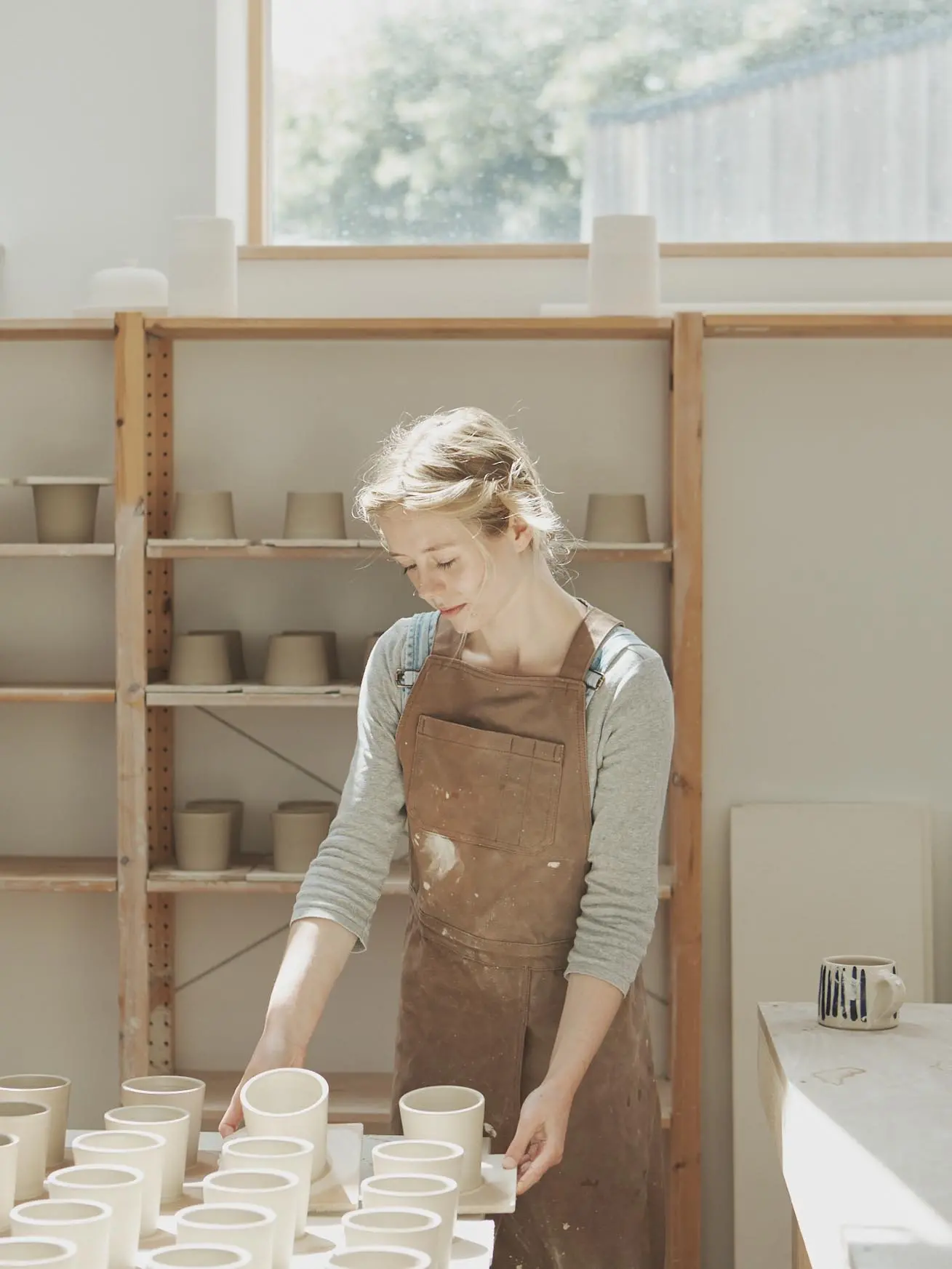 A female potter picking up freshly thrown ceramics from a worktable in her studio
