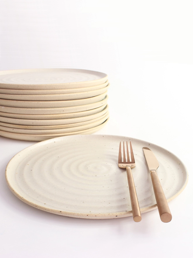 Large white dinner plate in foreground with cutlery, stack of plates in background