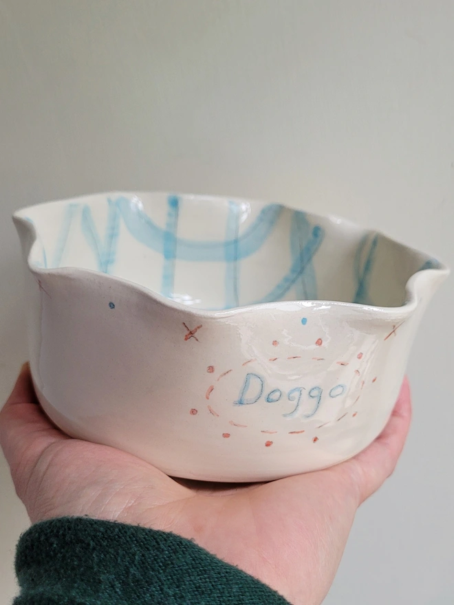 dog bowl held in a hand with the word doggo painted in blue with blue gingham check inside the dish
