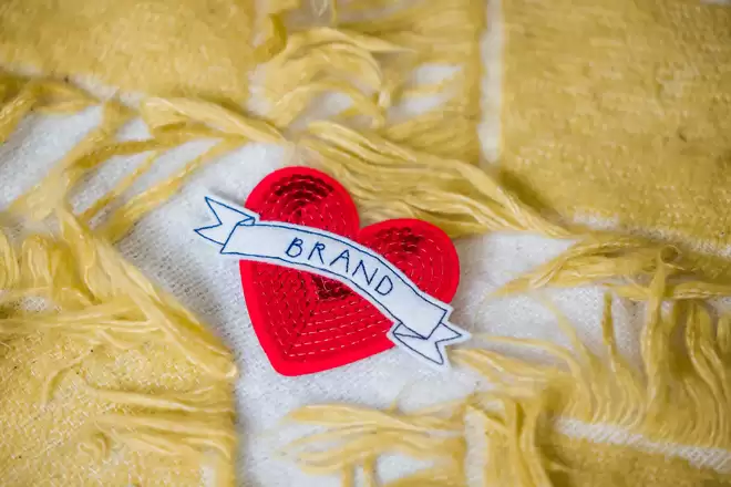 Red sequin heart with the word Brand across it on a yellow wool-background. 