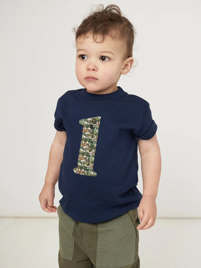 a 1 year old little boy wearing a navy t-shirt with a number one on the front depicting vintage cars on his first birthday 