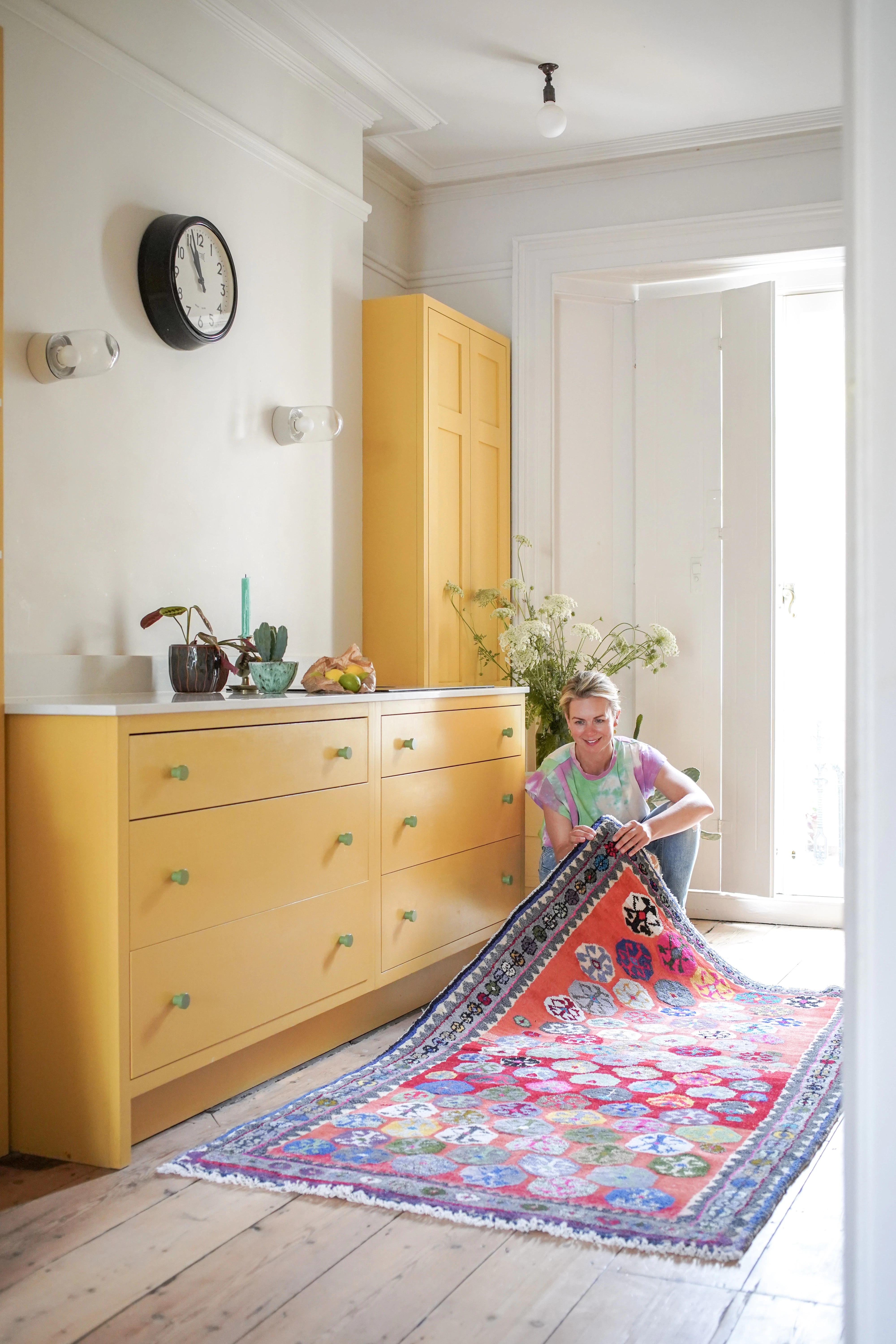 Female founder of UK business in yellow kitchen showing her colourful vintage rug collection