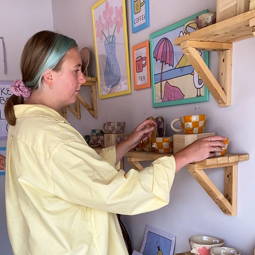 A photo of Katie organising a display shelf of her ceramics.