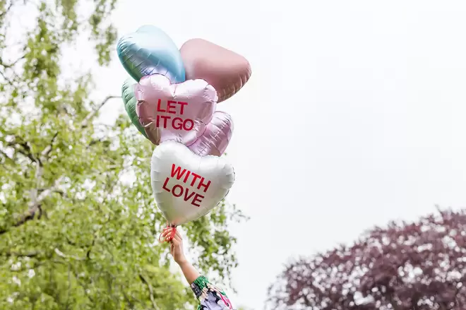 Let it go with love on hear-shaped balloons being held up outside 