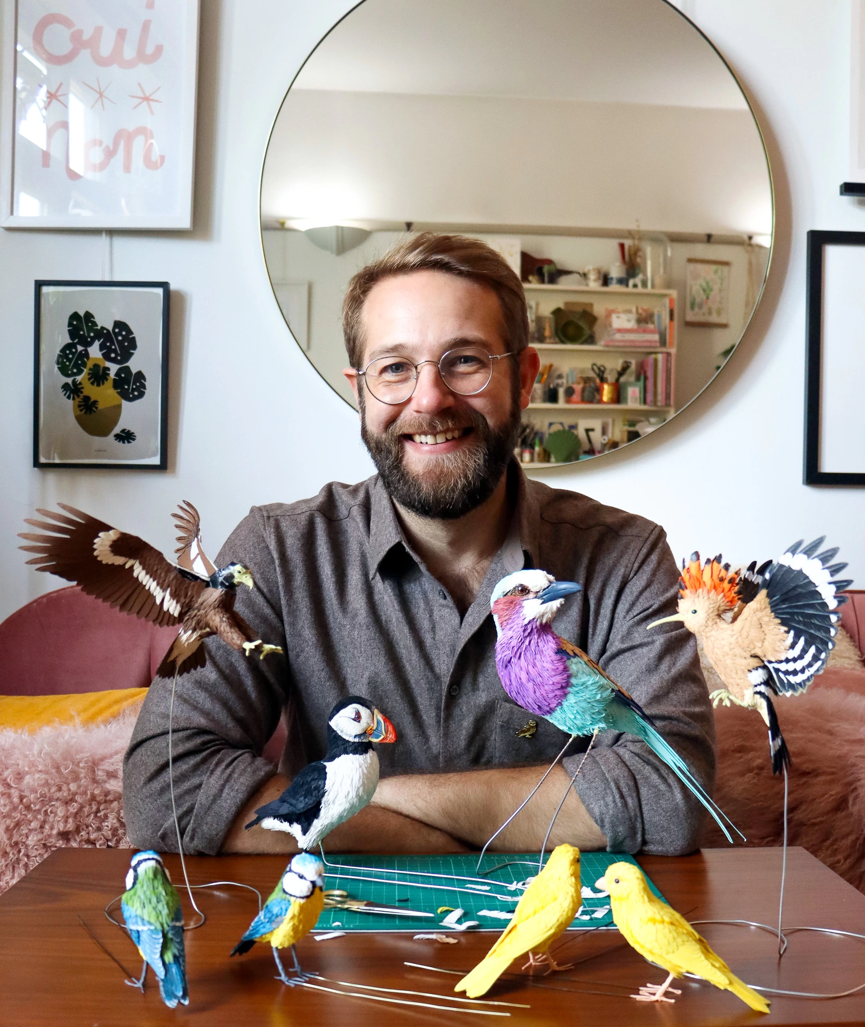 Zack Mclaughlin from Paper & Wood sat smiling  behind a few of his paper bird creations