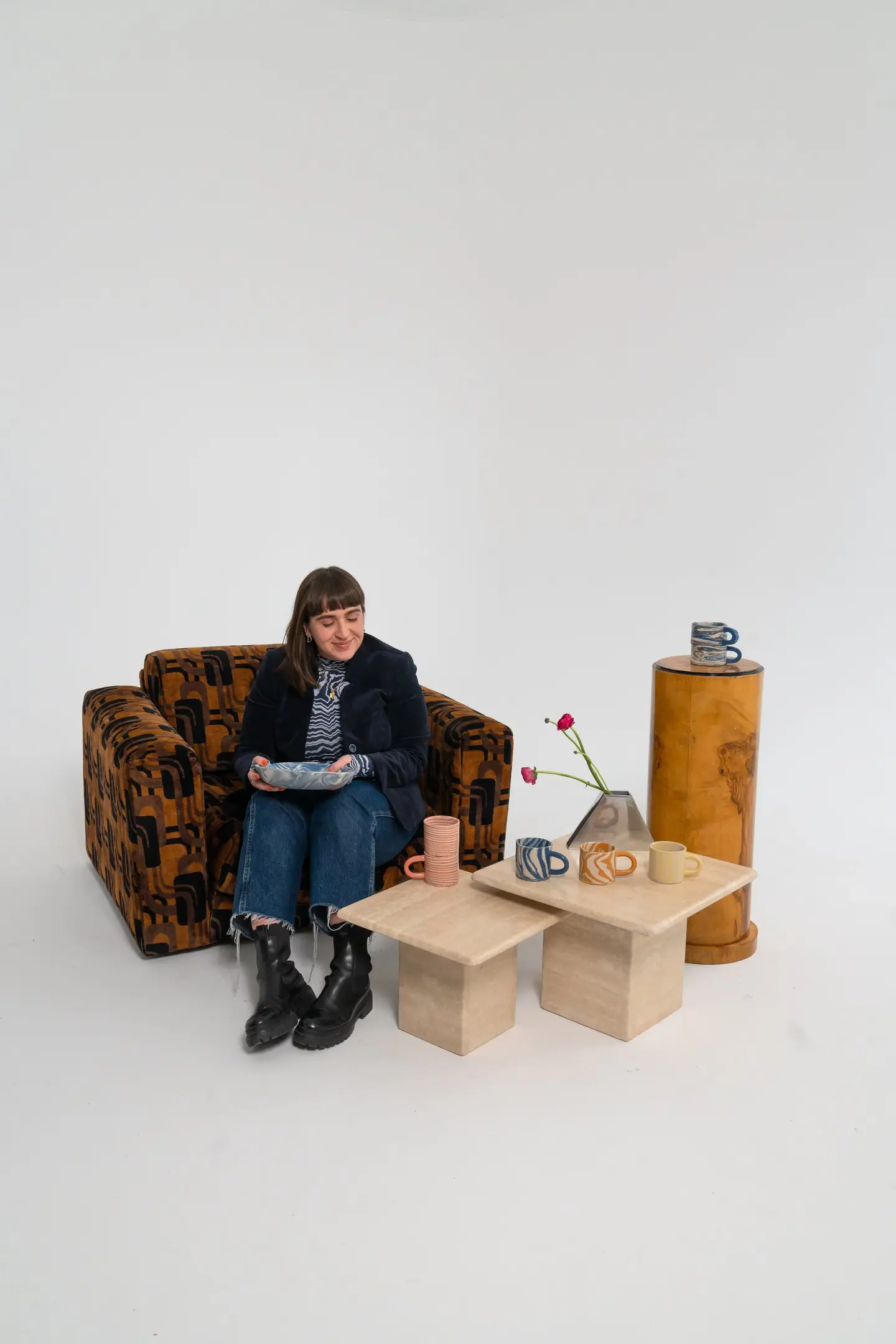 scarlett sitting on a couch, with two wooden tables and a pedestal each holding some PLOP Pottery pieces