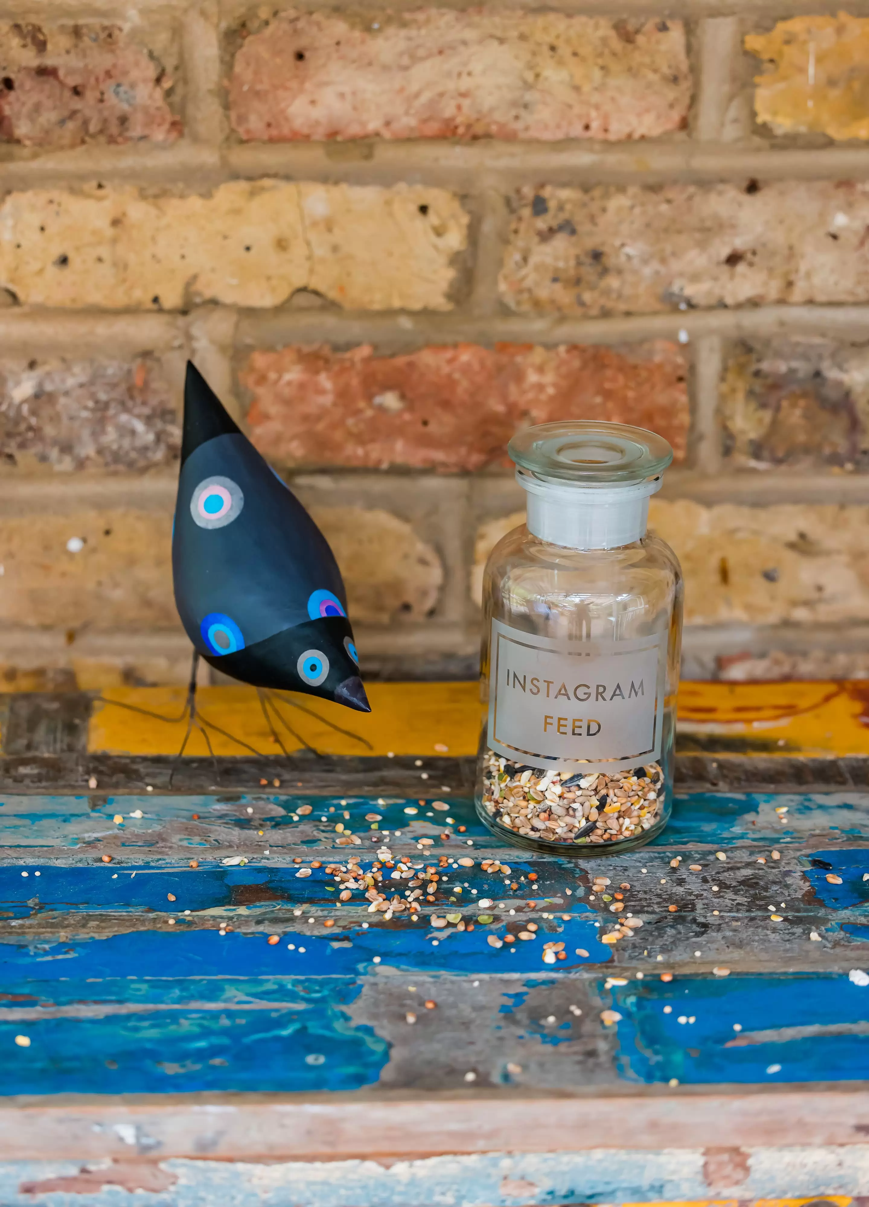Apothecary bottle containing bird seed engraved with words Instagram Feed with paper bird sitting next to it 