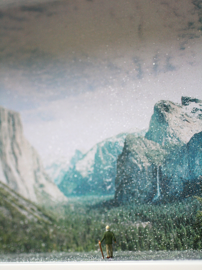 Miniature scene in an artbox showing a tiny man hiking towards a sparkling mountainous backdrop. 