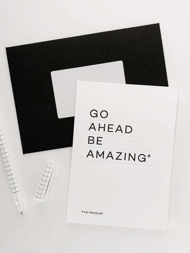 Be Amazing Good Luck Card laid on a black and white envelope next to a white pen.